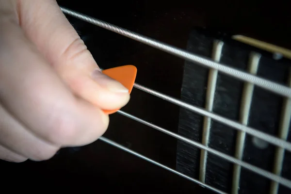 Bass guitar player with pick in his hand closeup, technique lesson and practice theme. Playing on bass electric guitar, live music and skill concept. Close view of guitarist fingers and bass strings.