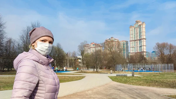 Woman with surgical mask on face in city park during COVID-19 coronavirus pandemic. People wearing medical mask on street due to coronavirus disease. Concept of quarantine and corona virus outbreak.