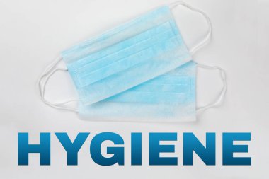 Coronavirus önleme. İki tipik 3 katmanlı mavi cerrahi maske üzerine HYGIENE metni beyaz arka planda üst üste yatıyordu. Hijyen Corona virüs koruma konsepti. Düz yatıyordu.