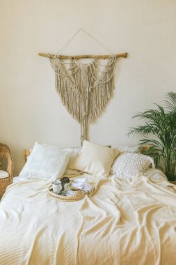 Modern romantik scandi boho tarzı yatak odası dekoratif yastıklar, yeşil bitki ve diy makrome duvar paneli. Ilık, rahat bir ev. Jomo, hafta sonu kahvaltısı yatakta..