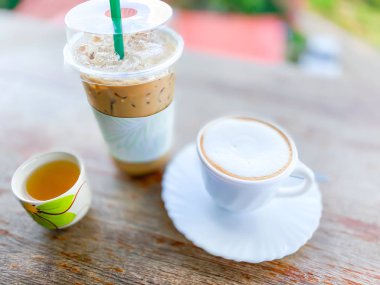 Sıcak ve buzlu kahveyi ahşap masaya koy ve arka planda iç.