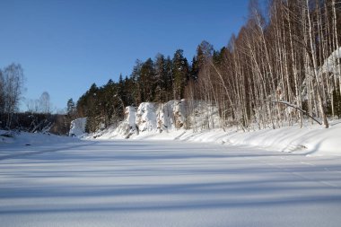 Karla kaplı uçurumlar buzlu nehir kıyısında.