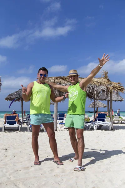 Two men are standing side by side on the beach, flapping their arms in a racial gesture.