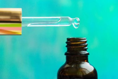 Renkli arka planda kozmetik yağ damlaları olan kozmetik pipeti. Cam damlacıktan dökülen temel yağ. Temel yağ, hyaluronik asit. Omega-3. Bitkisel özler.