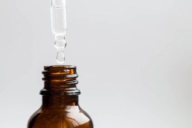 Beyaz arka planda izole edilmiş kozmetik yağ damlalarıyla kaplanmış kozmetik pipeti. Cam damlacıktan dökülen temel yağ. Temel yağ, hyaluronik asit. Omega-3. Bitkisel özü.