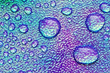 Cilde damlatıyor. Yapay deri. Su damlalarına yakın çekim. Yüzeyinde damla olan soyut mor ve mavi ıslak doku.