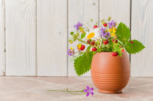 Morangos maduros e um buquê de flores da floresta em uma caneca de barro — Fotografia de Stock