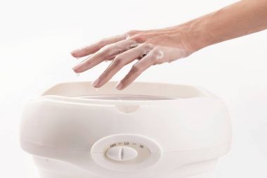 Manikürcüdeki kadın manikür yaptırıyor, ellerini parafinle ya da balmumuyla yıkıyor. 