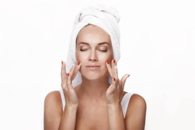 Beyaz bluzlu, duştan sonra kafasında havluyla güzel bir genç kız yüzüne krem sürüyor, masaj yapıyor ve gülüyor. Bir yüzü kremle nemlendirir. Spa mı? Stüdyoda, beyaz arka planda..