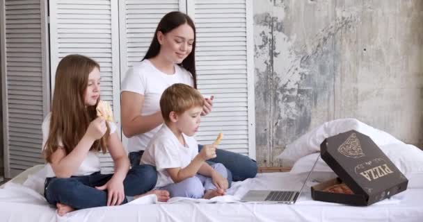 Mamá y los niños en auto-aislamiento comen pizza y ven dibujos animados en una computadora portátil — Vídeos de Stock