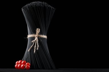 Siyah spagetti makarnası taze domatesli siyah arka planda çiğ..