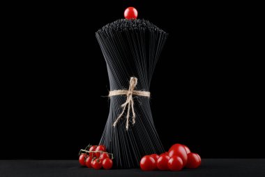 Siyah spagetti makarnası taze domatesli siyah arka planda çiğ..