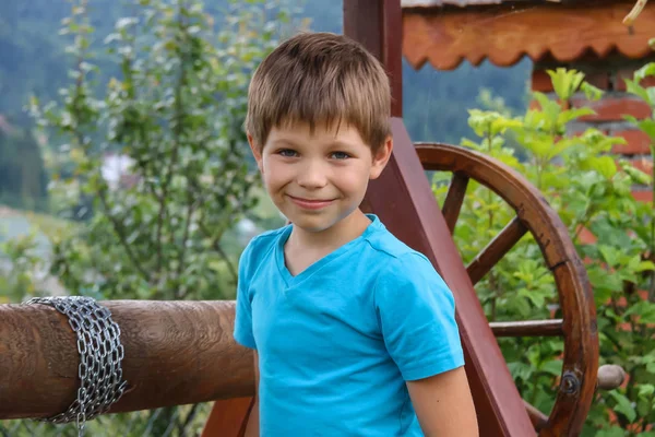 Muchacho sonriente delante del viejo pozo de madera de estilo —  Fotos de Stock