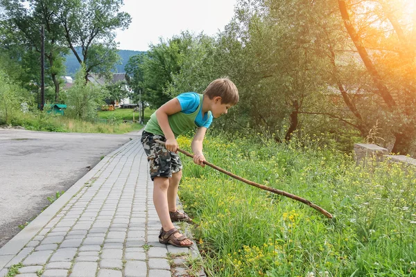 日光の道端に木の棒と遊ぶ少年 — ストック写真