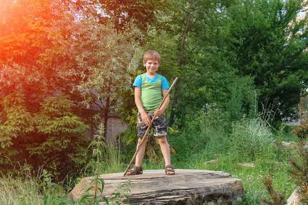 Smiling boy with stick on big stone in sunlight — Stock Photo, Image