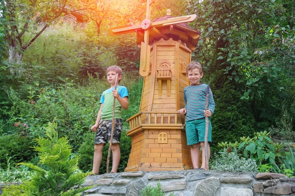 Two boys next to small mill in summer city park in sunlight — Stock Photo, Image