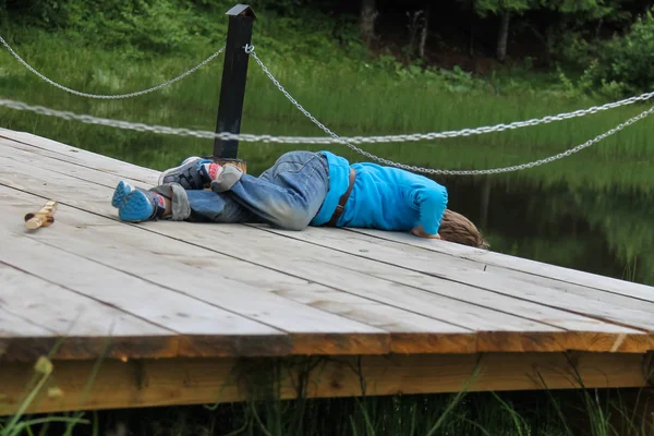 Pojken ligger på träbro vid sjön — Stockfoto