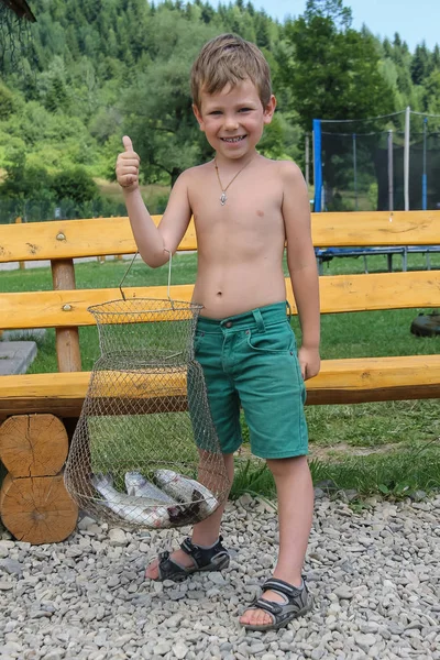 Leende pojke med färsk fångad fisk i sommar — Stockfoto