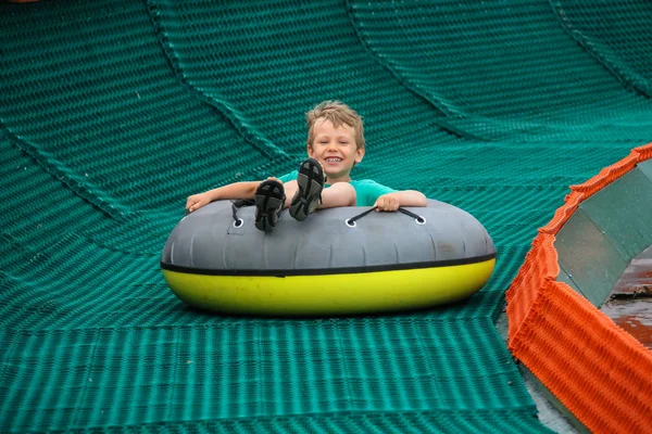 Sonriente niño se desliza hacia abajo en el anillo inflable — Foto de Stock