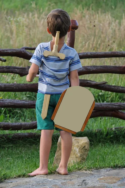 Junge mit Holzschwert und Schild steht vor Stein — Stockfoto