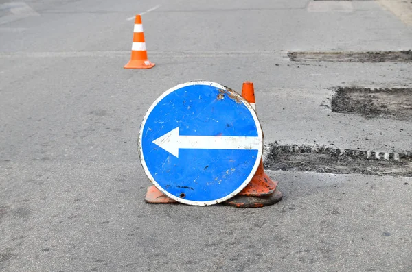 Road repairs. Plastic orange cone on the asphalt road. Detour sign on the street, roadworks. Restricted local government budgets are reflected in potholes and damaged roads. — Stock Photo, Image