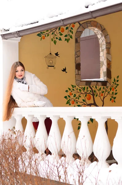 Das Mädchen mit den langen Haaren im Winter, sie im weißen Pelzmantel. sie steht auf dem balkon — Stockfoto