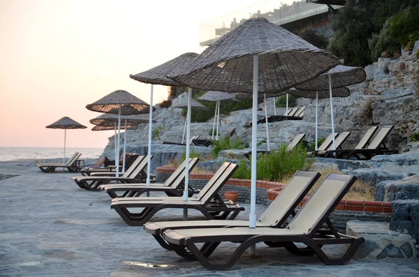 Beach with sunshades and sunbeds against the backdrop of the picturesque bay of blue sea and mountains. Sunbeds on the beach in Turkey on the beach