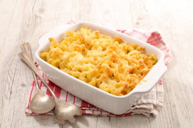 Ahşap masa üzerinde kaşık ile beyaz seramik pişirme çanağı peynirli makarna pişmiş