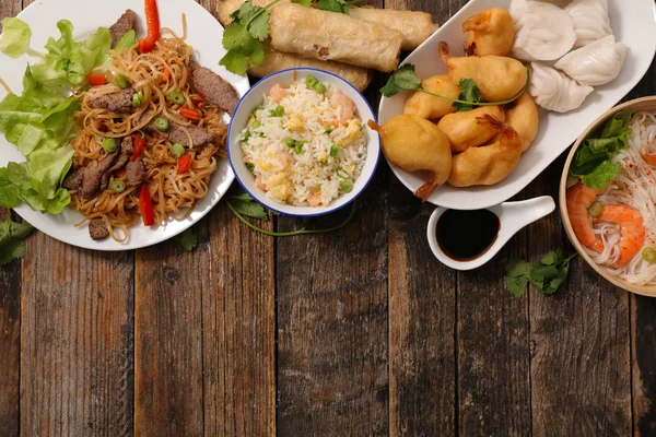 assorted chinese food, noodle, rice, spring rolls shrimps and sauces on wooden table