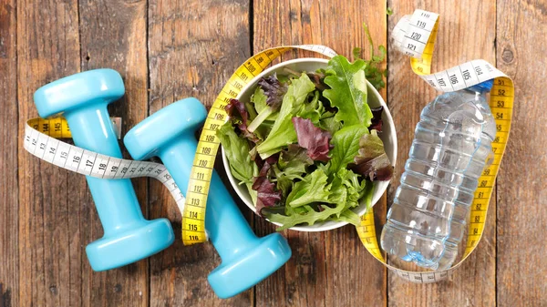 bowl with salad and water bottle with measuring tape and dumbbells, healthy food concept