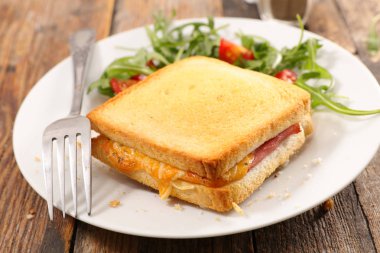 Jambon ve beyaz çatal, roka ve domates ile tabakta çedar peyniri ızgara tost.