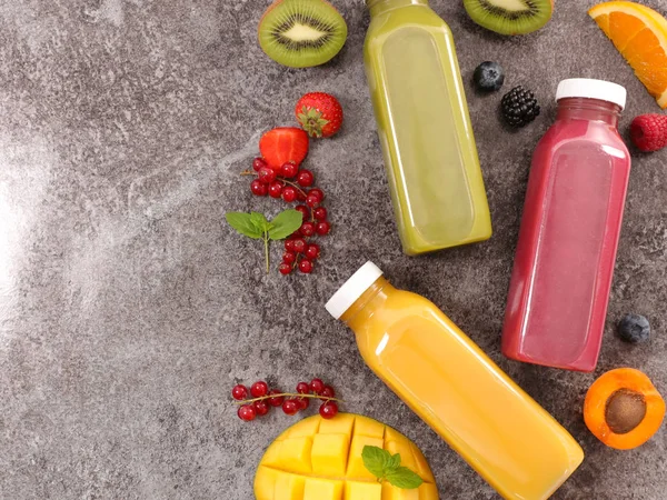 Bottles with fruit juice with fruits around on stone background