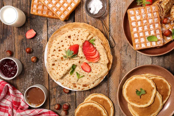 Set of pancakes, crepes and waffles with nuts, sauces and berries on wooden table