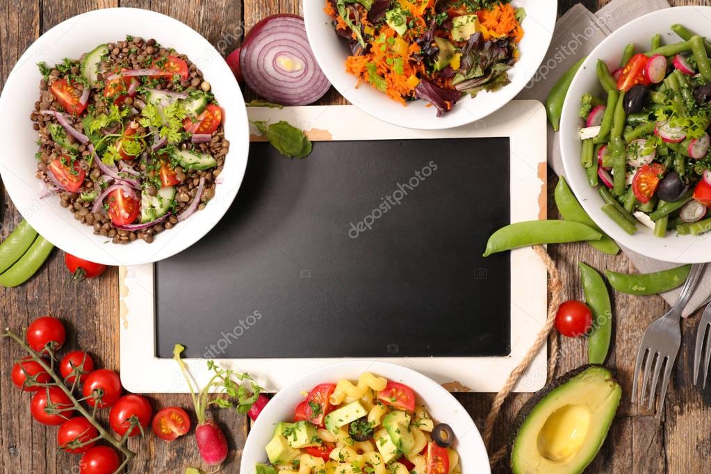 selection of healthy vegetable salads around chalkboard 