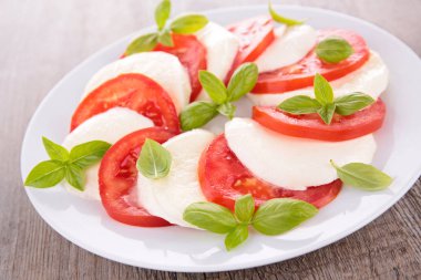 Fesleğenli ahşap masa üzerinde beyaz tabakta servis Caprese salatası