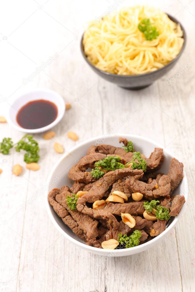 Delicious fried beef with peanuts and pasta in plates on wooden table