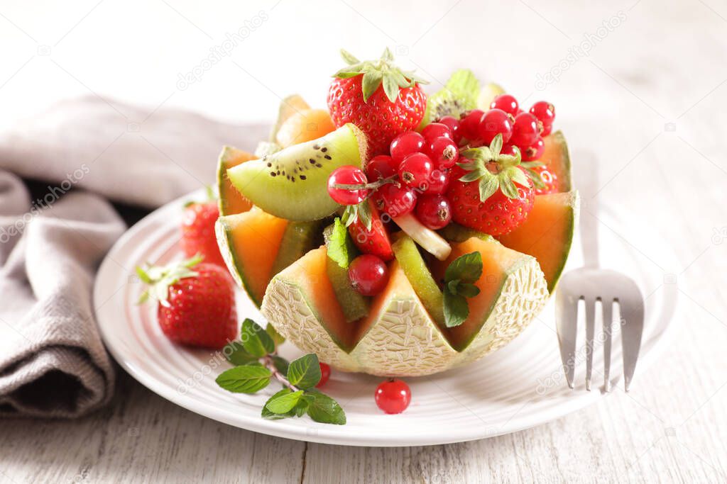 fruit salad in melon bowl with berry fruit, kiwi and banana