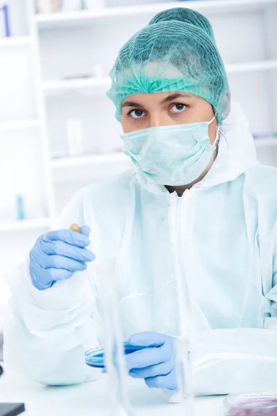 Medicul în mănuși de protecție și mască chirurgicală și pălărie în comparație cu lichidul din laborator . — Fotografie, imagine de stoc