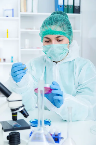 Arts in beschermende handschoenen en chirurgische masker en muts vergelijken met vloeistof in laboratorium. — Stockfoto