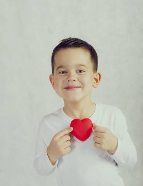 Bir kırmızı kalp heykelcik tutan beş yaşında boy gülümseyerek