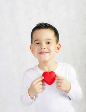 Bir kırmızı kalp heykelcik tutan beş yaşında boy gülümseyerek
