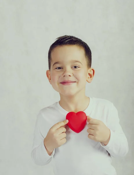 Bir kırmızı kalp heykelcik tutan beş yaşında boy gülümseyerek