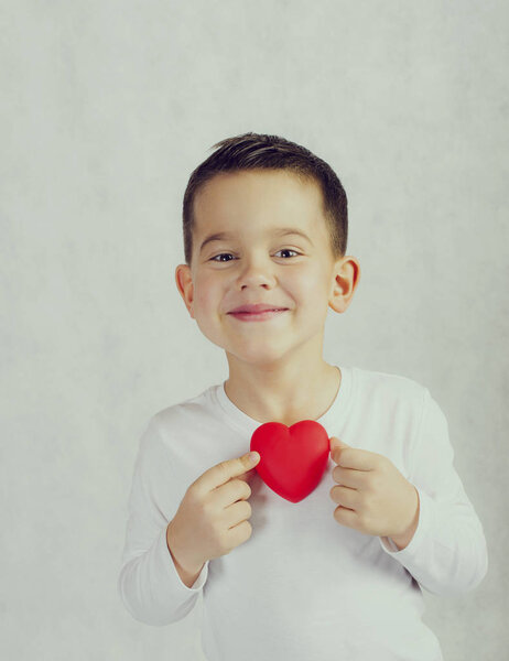Пятилетний улыбающийся мальчик держит в руках фигурку красного сердца
