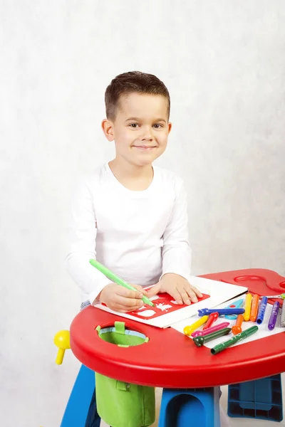 Chico dibuja sentado en el escritorio de los niños — Foto de Stock