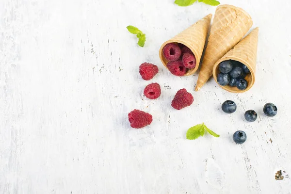 Summer berries, raspberries and blueberries in waffle cone on blue and white wooden background