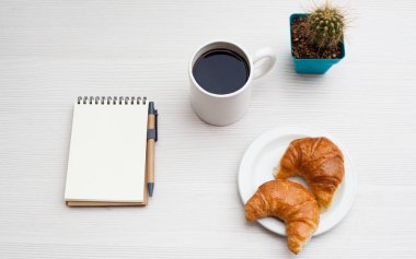 Üstten Görünüm Ofis Masası. Defter, kahve ve kruvasan beyaz masada.