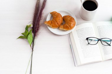 Üstten Görünüm Ofis Masası. Kitap, kahve ve kruvasan beyaz masada.