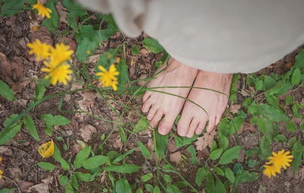 Pernas de mulher em pé no chão com grama e flores — Fotografia de Stock