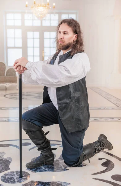 Храбрый человек в средневековой одежде с тростью, стоящей на коленях — стоковое фото