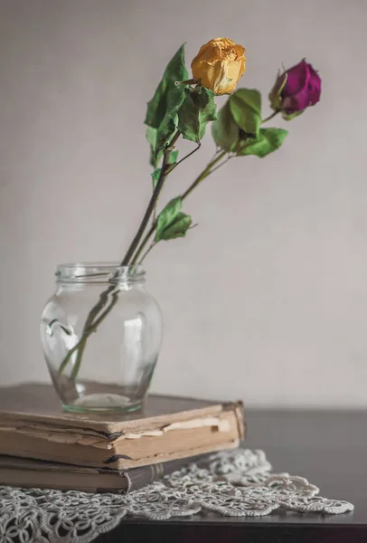 Still life with dry roses in glass bottle on vintage lace and ol — Stock Photo, Image